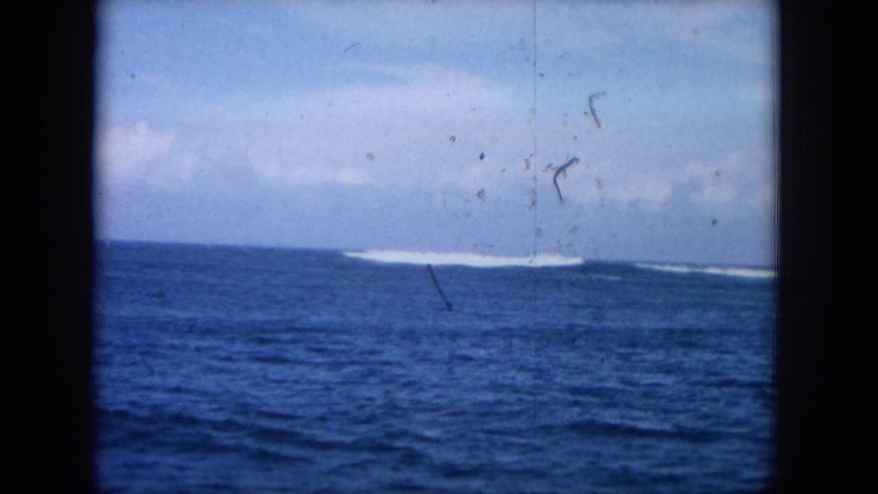 Blue ocean and distant white surf seen through a dark window frame.