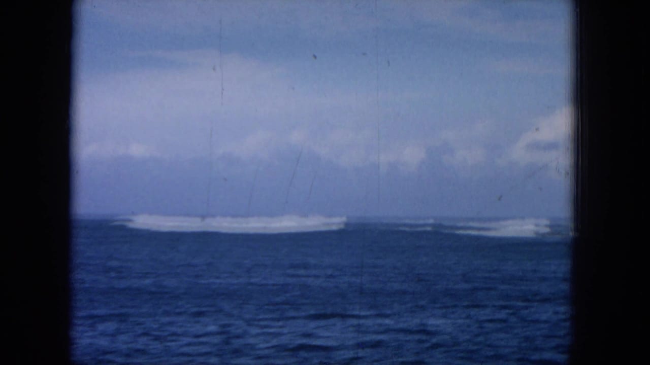 Open sea with a long white surf break under a partly cloudy sky.