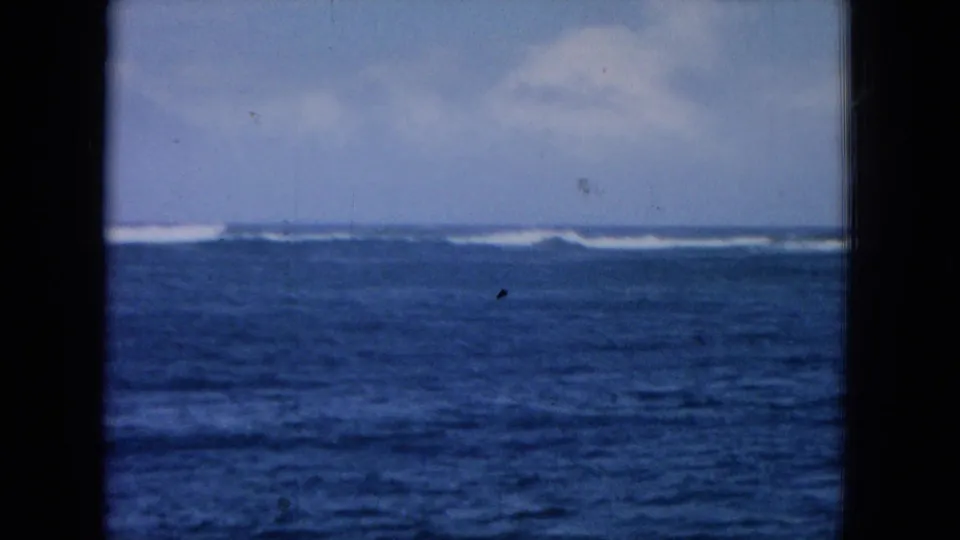 1964 Hawaii coastal travel frame with choppy blue water, distant white breakers, soft sky, and visible film wear.