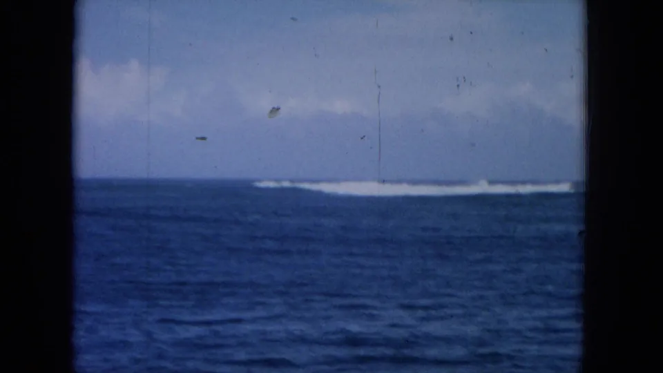 A 1964 Hawaii 8mm frame shows offshore whitecaps, blue sea, cloudy sky, and dark borders from the viewing window.