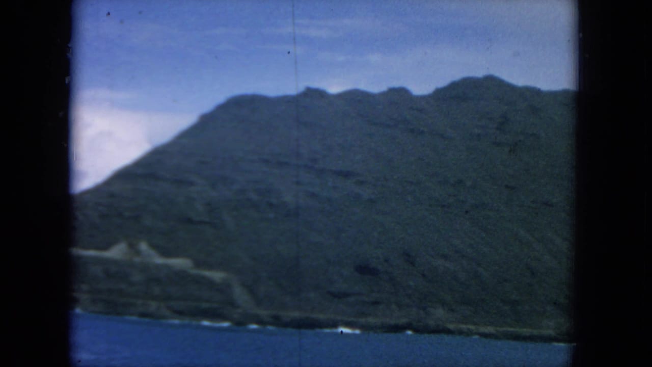 Green mountain slope rising above blue ocean, seen through dark 8mm film borders.
