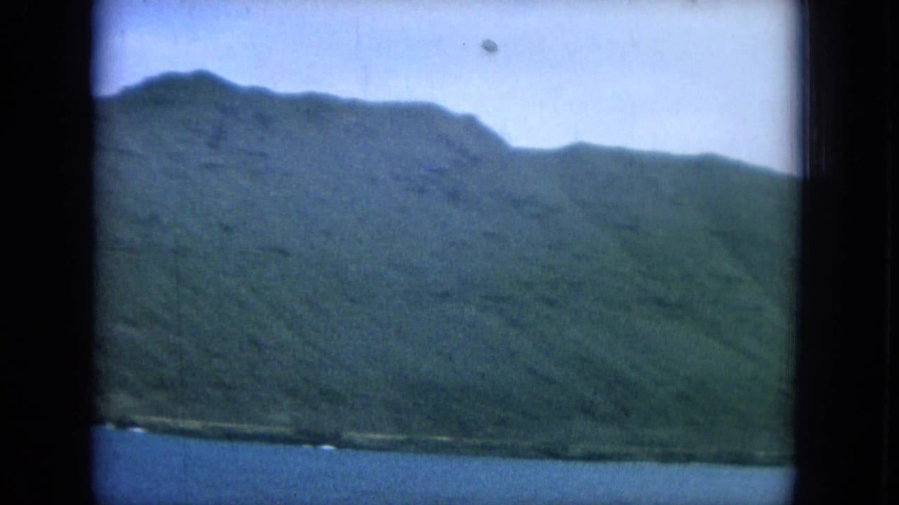 Mountain ridge and shoreline above ocean water, framed by dark film edges.