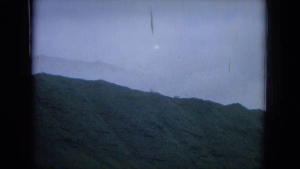 1964 Hawaii home-movie frame of a green ridge under overcast sky, with slight lens flare and film wear visible.