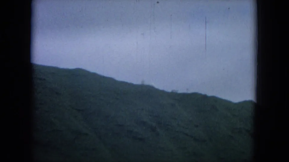 1964 Hawaii 8mm view of a sloping green hillside, with dust marks and soft home-movie exposure visible.