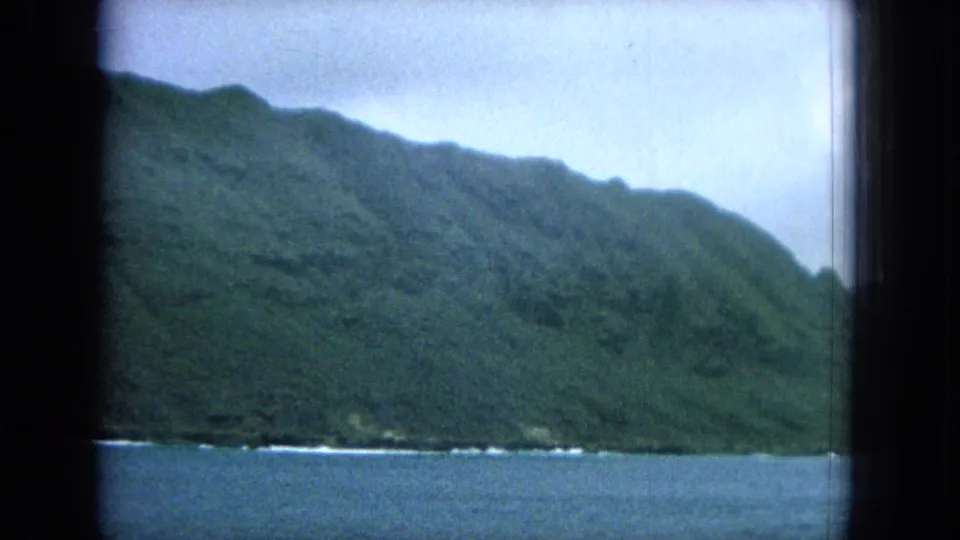 1964 8mm Hawaii coastal landscape from a boat, showing dense green slopes above the ocean and cloudy light.