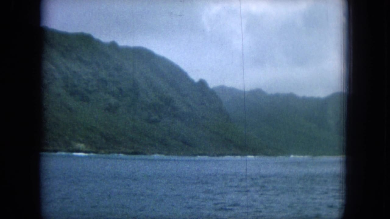 Blue ocean below steep green coastal mountains under cloudy sky.