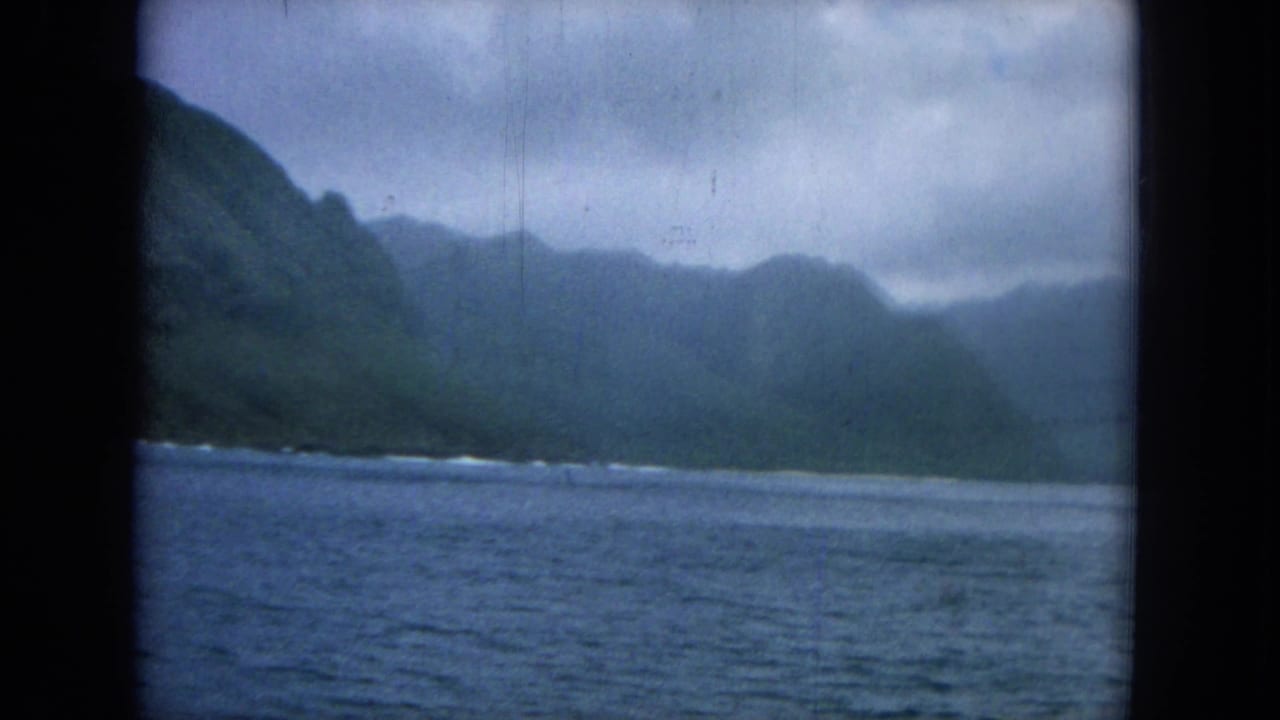 Distant green mountain coastline across blue water with dark film borders.