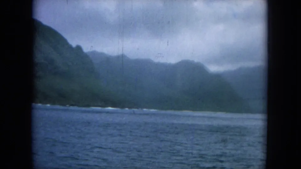 Offshore view of a green mountainous Hawaii coastline across blue water, framed by dark 8mm gate edges.