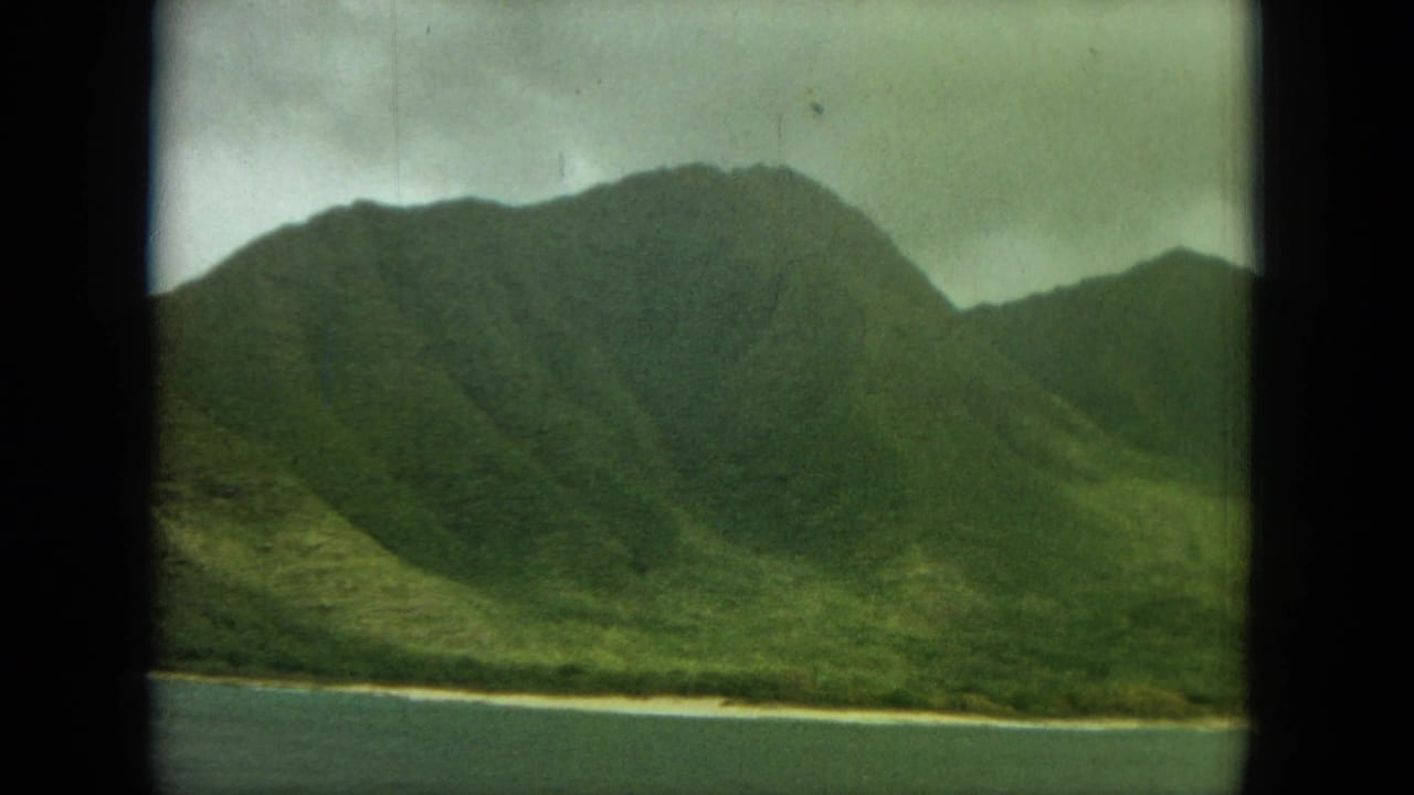 Steep green mountain ridge beside water, with a dark vertical divider in the foreground.
