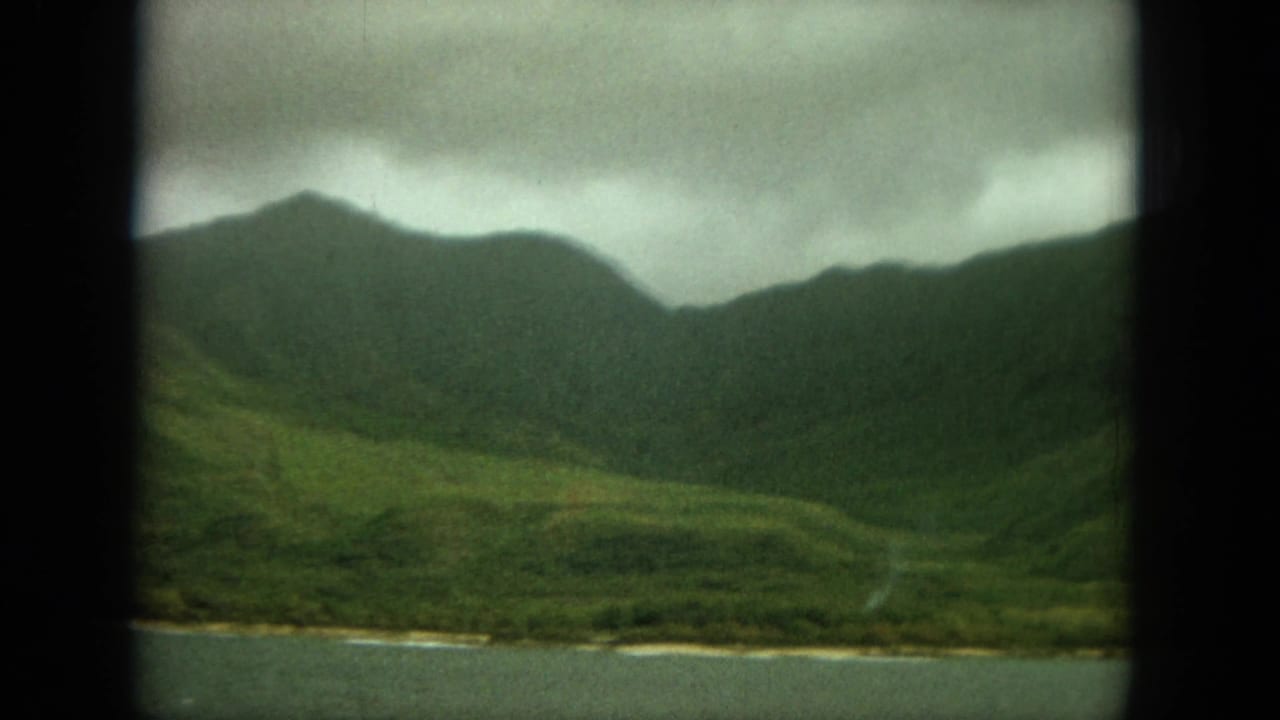 Green mountain ridge above coastal water, framed by dark film borders.