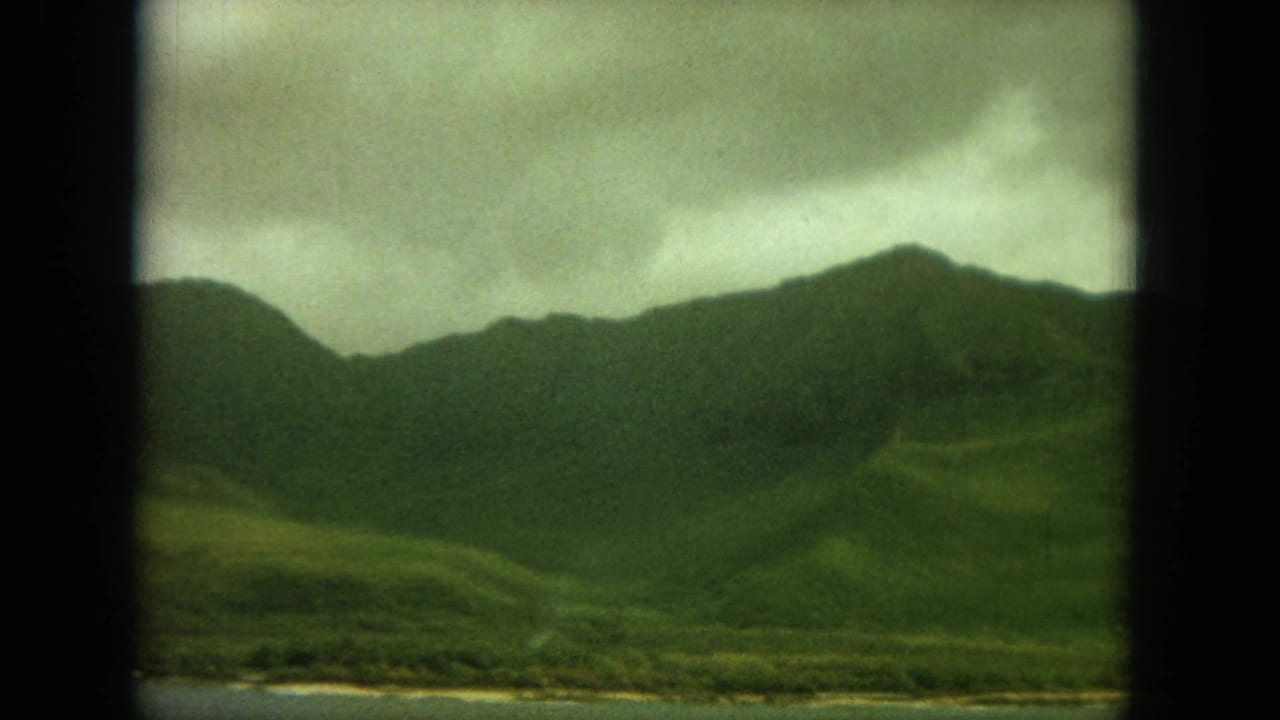 Dark-framed view of green hills and a narrow coastline under cloudy sky.