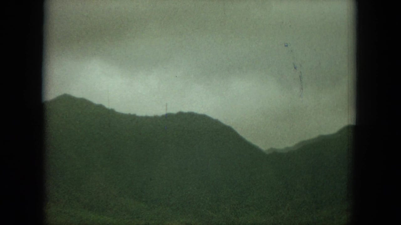 Dark mountain ridge beneath a pale overcast sky, framed by 8mm film borders.