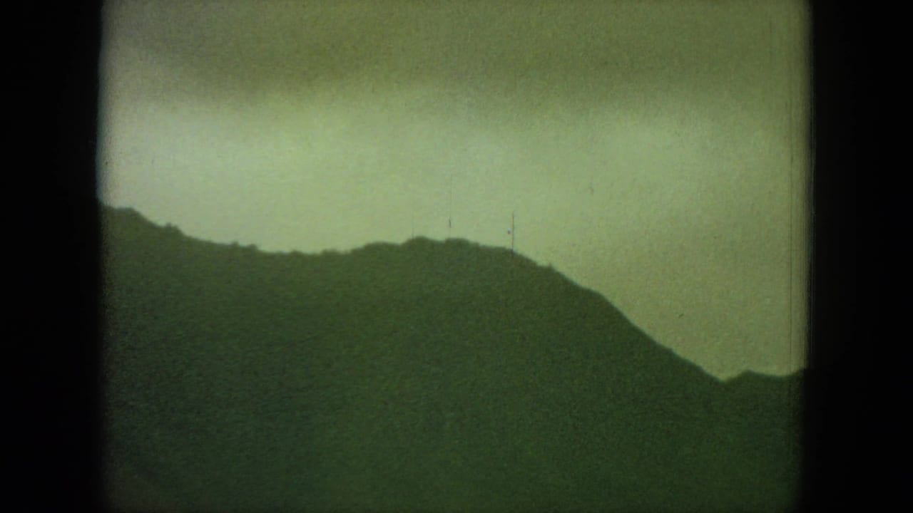 Darker mountain slope under a pale sky with heavy film grain and edge borders.