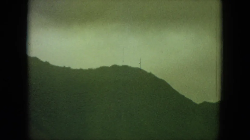 1964 Hawaii home-movie frame with a dark mountain profile against a muted overcast sky.