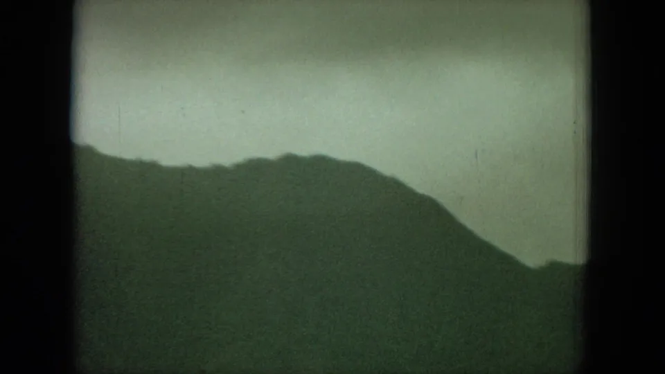 1964 Hawaii 8mm footage frame showing a closer mountain ridge with soft grain and muted sky.