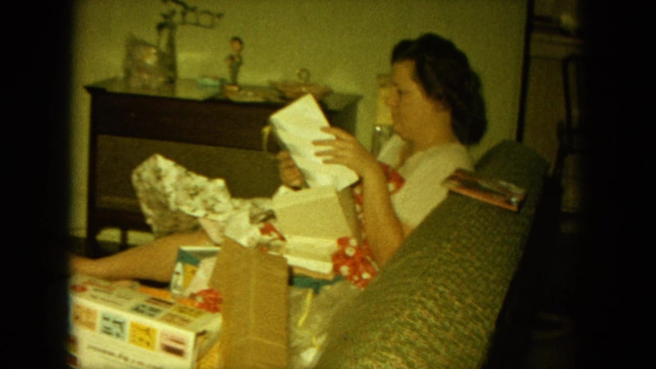 Woman seated on a couch opening a wrapped Christmas gift in a living room.