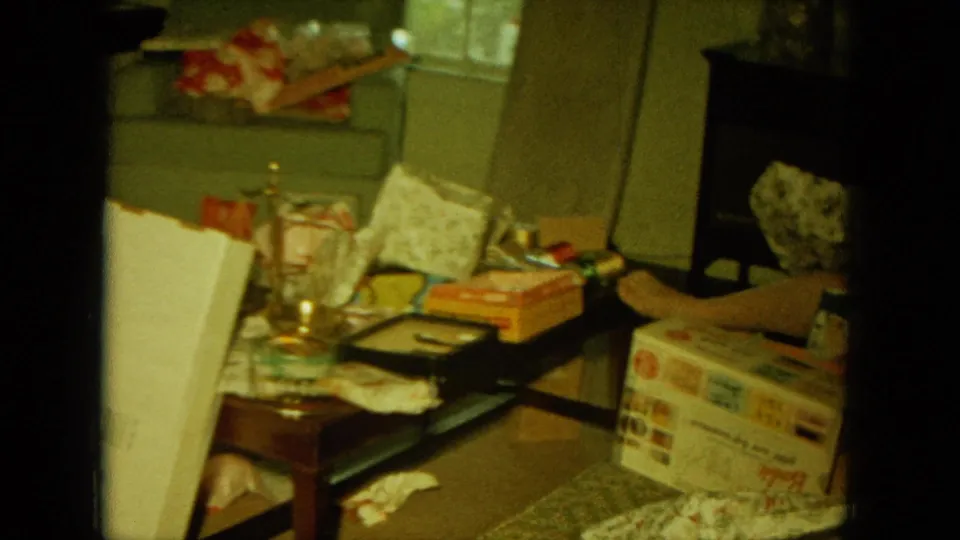 The final frame shows a living-room table with holiday packaging, glasses, boxes, and part of the seated woman at the edge.