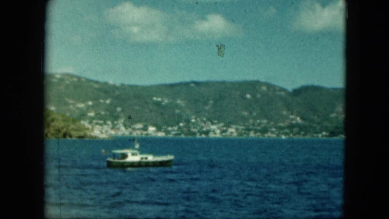 Motorboat on darker blue water with hillside shoreline and clouds in the distance.