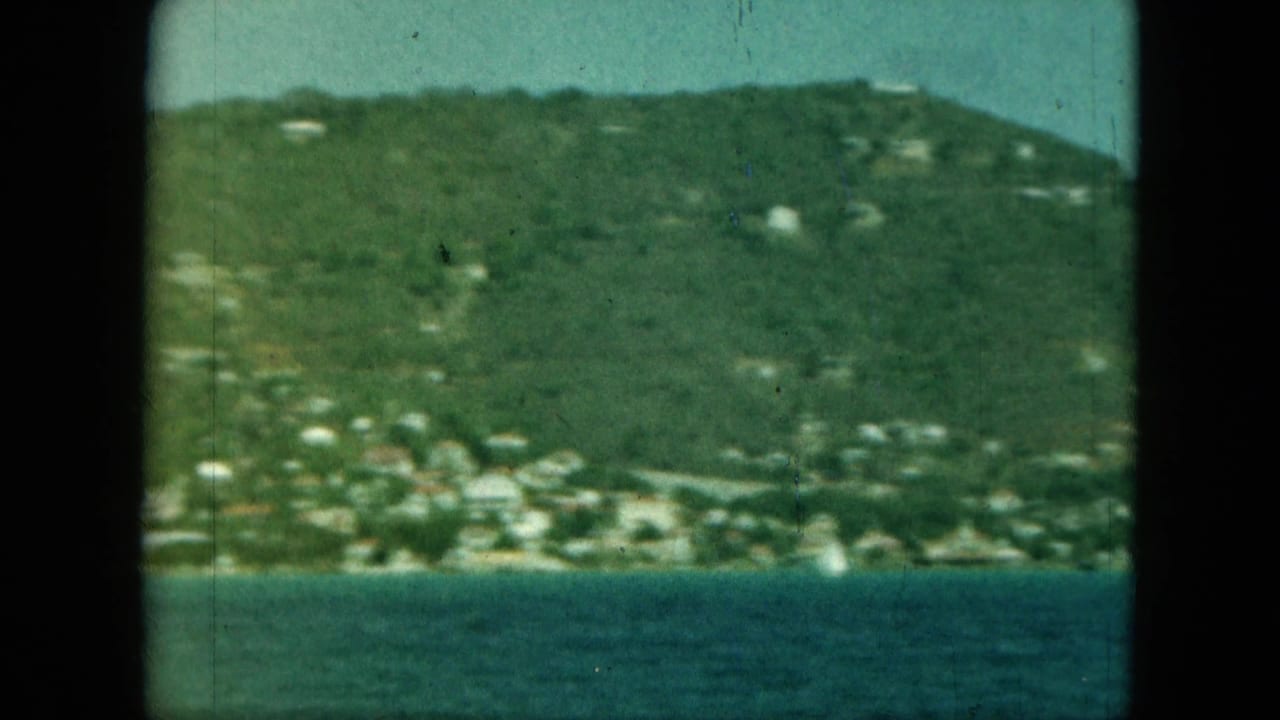 Green hillside with scattered pale buildings across blue-green bay water.