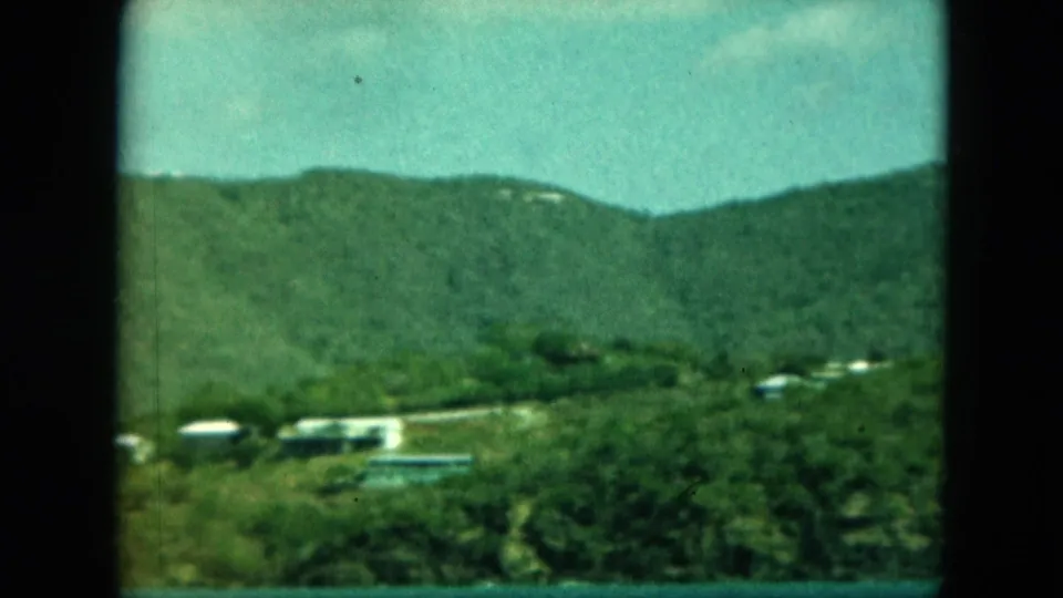 1964 8mm view of lush Saint Thomas hills with small white buildings below a blue-green sky.