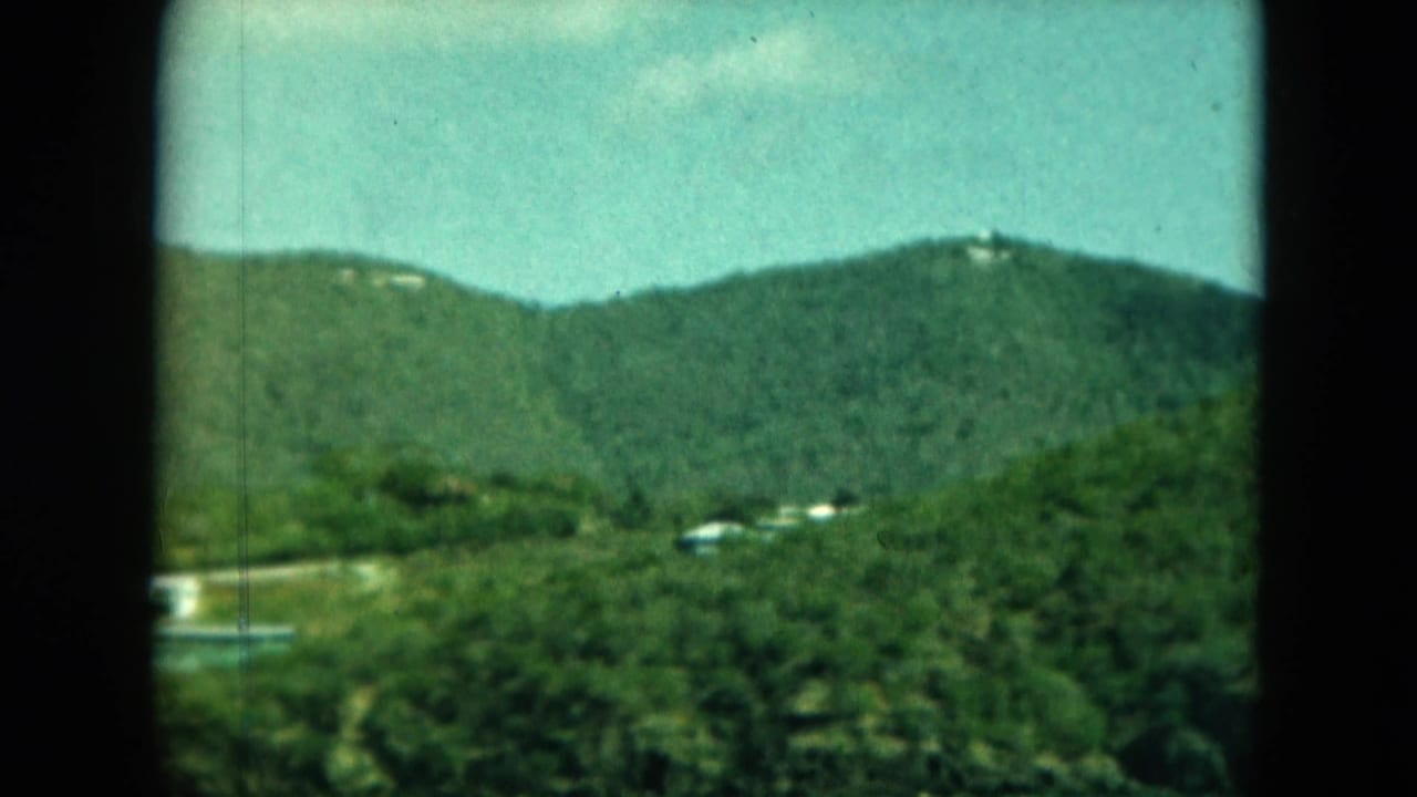 Distant green hillside with small white structures and dark film borders.
