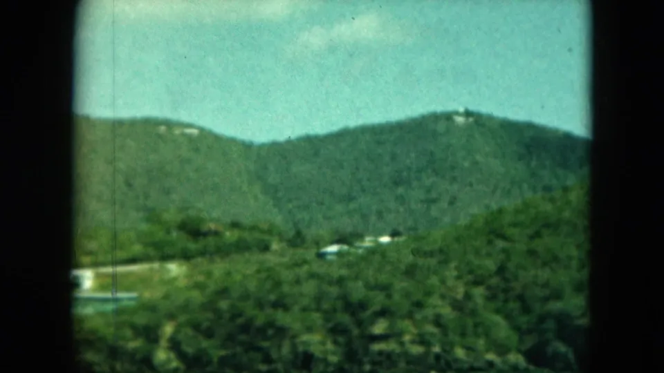 Distant Saint Thomas hillside with white buildings scattered through tropical greenery in soft 8mm color.