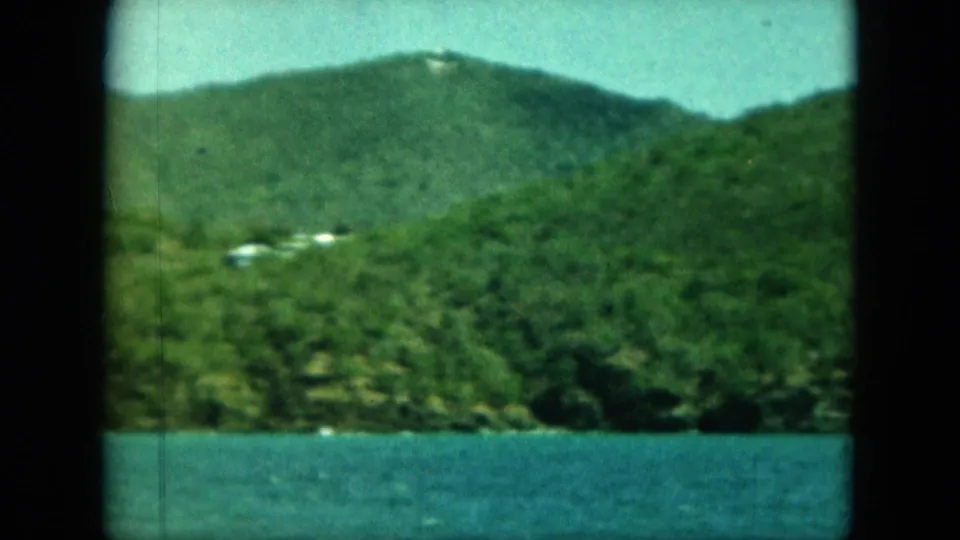 Saint Thomas shoreline view with blue water in the foreground and green hillside buildings beyond.
