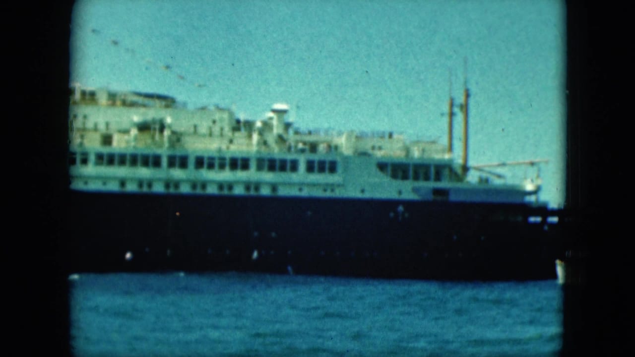 Passenger ship broadside with white decks, dark hull, and a mast against blue sky.