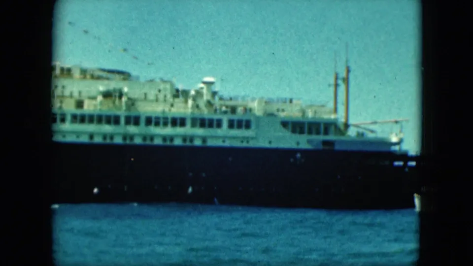 1964 8mm frame showing the passenger ship's middle section at port, with rows of windows, dark hull, and open sky.