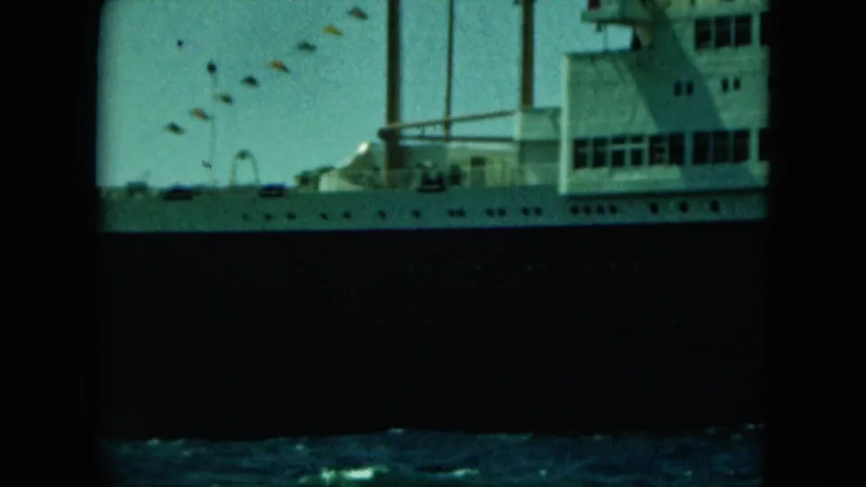 1964 8mm view of part of the cruise ship, with white deck structures, vertical mast lines, and water in the foreground.