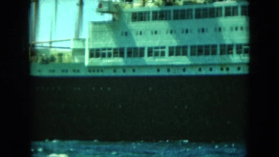 1964 8mm frame showing the cruise ship's white superstructure and dark hull from a waterside viewpoint.