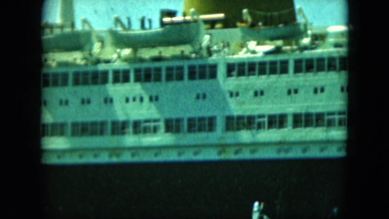 Large passenger vessel midsection in soft 8mm color, with lifeboats, deck railings, windows, and tiny people visible on deck.