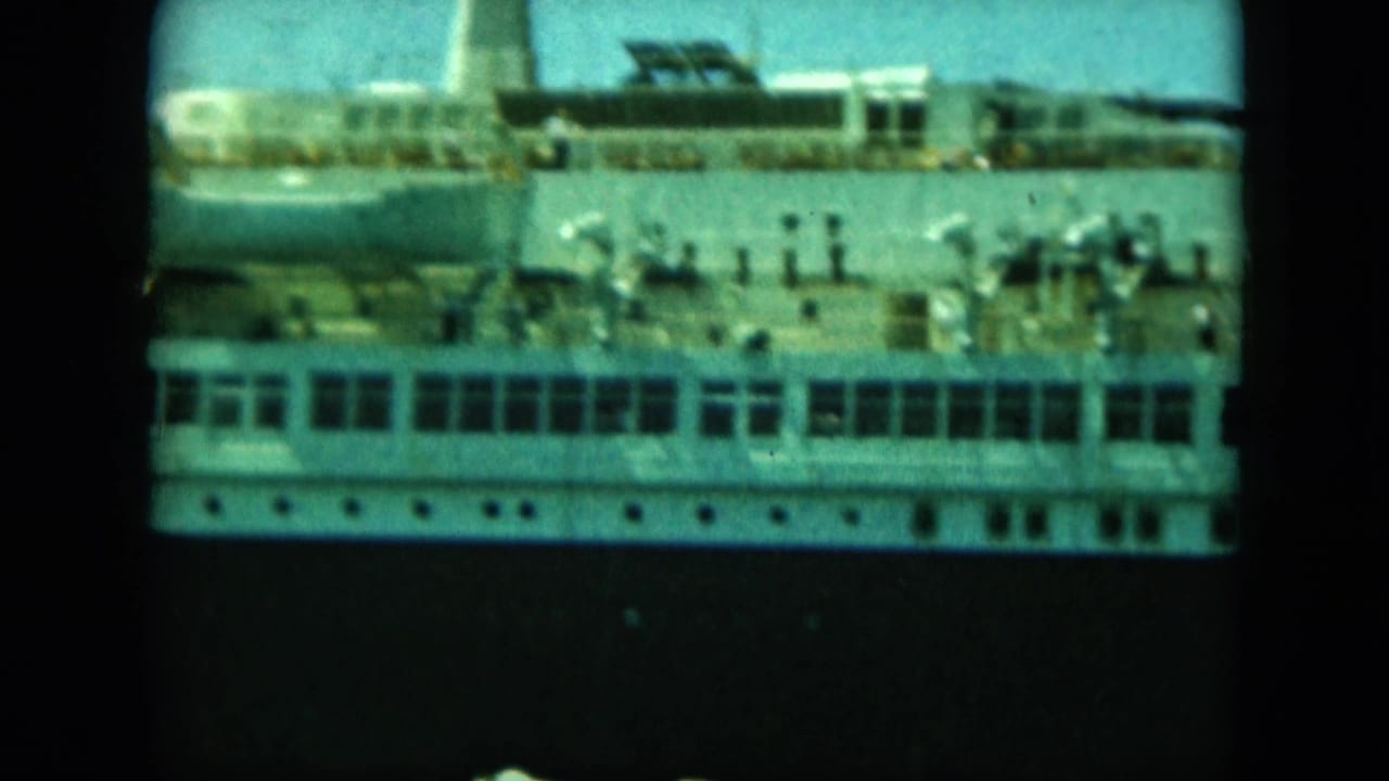 A large white passenger ship fills the frame, with rows of windows, deck railings, and small people visible on the upper deck.