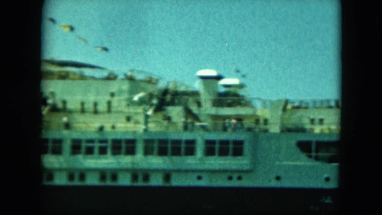 The camera frames the upper decks of a white cruise ship, with distant people, deck equipment, and bright sky above.