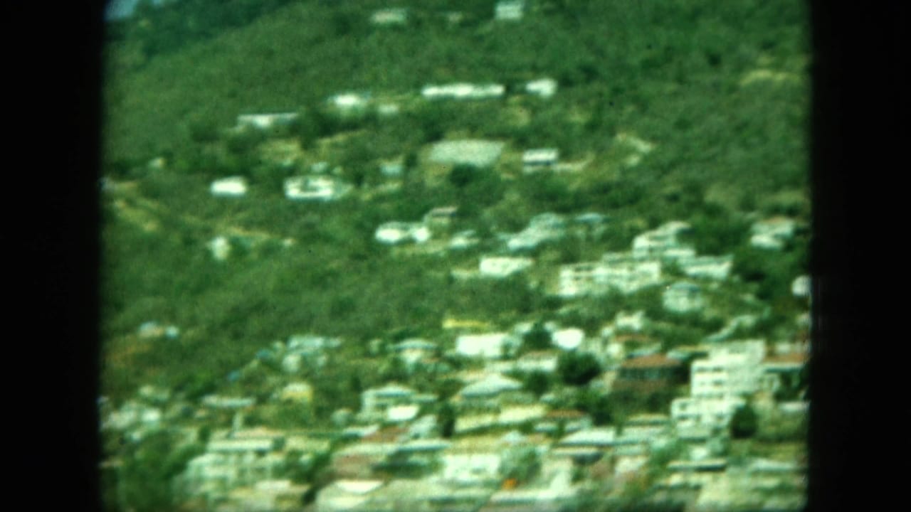 Distant hillside town above a waterfront, seen through dark film frame edges.