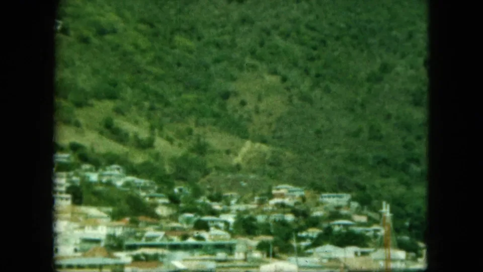 1964 8mm frame of a coastal settlement identified by metadata as Saint Thomas, with hillside homes above the waterfront.