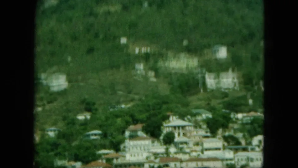 Soft, blurred 8mm view of Saint Thomas hillside development with pale buildings, vegetation, and a strip of harbor water at the edge.