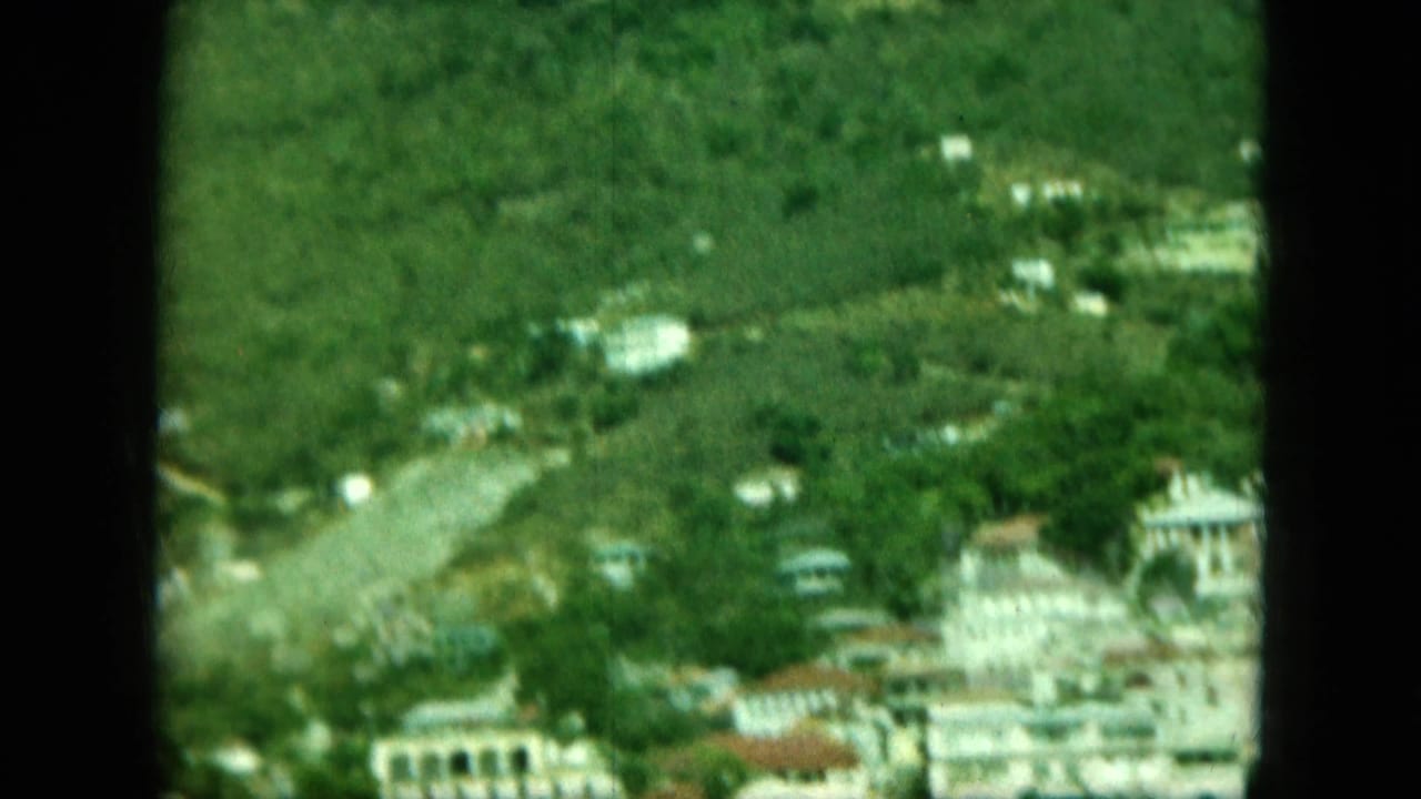 Coastal hillside town with white buildings, roads, trees, and dark 8mm frame bars.