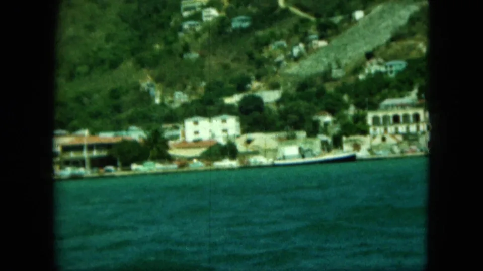 Late frame of the clip with blue water in front, hillside buildings beyond, and dark 8mm frame edges around the view.