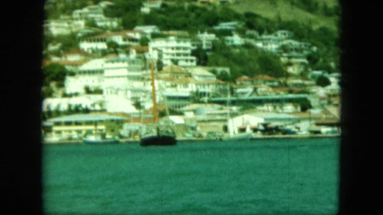 Coastal buildings beside turquoise water with a dark boat mast in front.