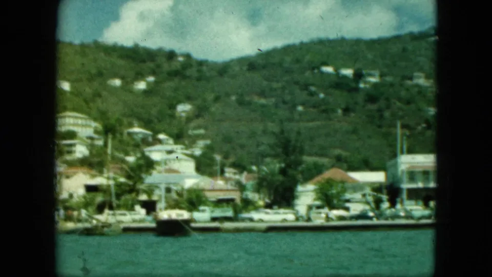 A similar harbor view shows hillside houses, small boats near shore, and a tropical waterfront under bright sky.