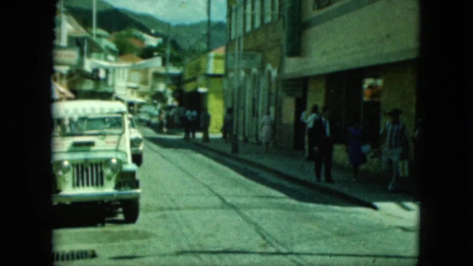 The closing frame shows the white jeep lower in the street, pedestrians at the right sidewalk, arched storefront details, and hills beyond.