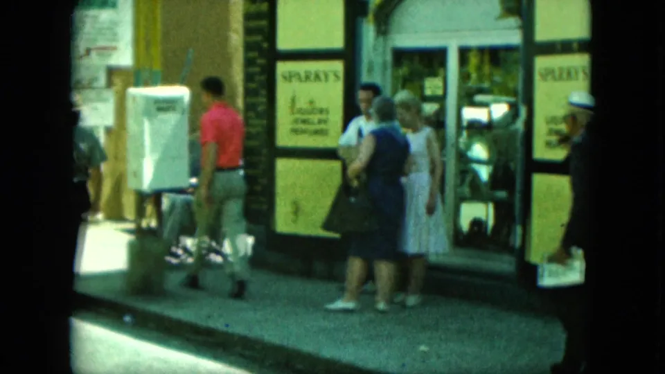 Several pedestrians gather outside a storefront marked SPARKY'S, with shop windows and sidewalk activity visible in the 8mm frame.