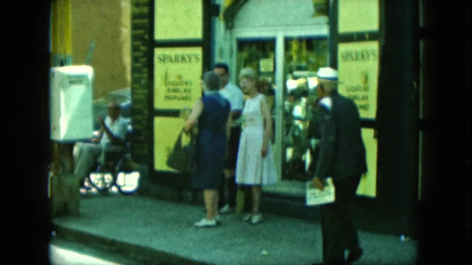 1960s 8mm frame of pedestrians outside a city storefront with Sparky's window signs for liquor, jewelry, and perfume.