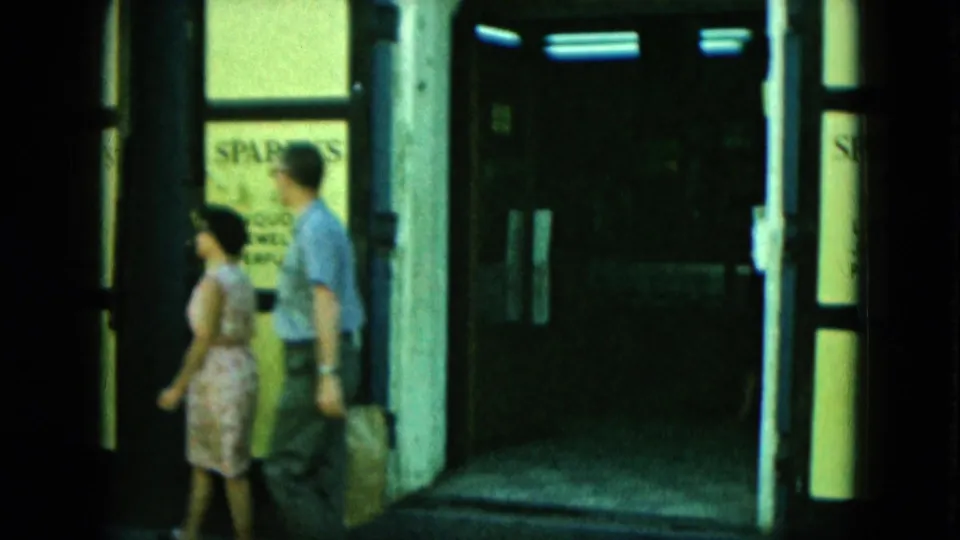 A couple walks past a dark storefront entrance, with part of a Sparky's window sign visible behind them.