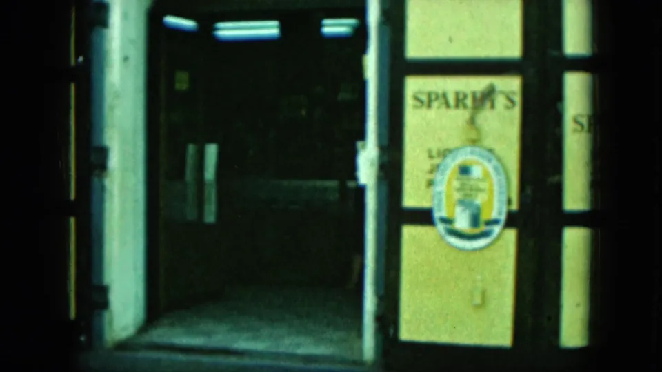 Storefront detail showing a dark entrance, Sparky's window sign, and a circular door emblem beside the sidewalk.