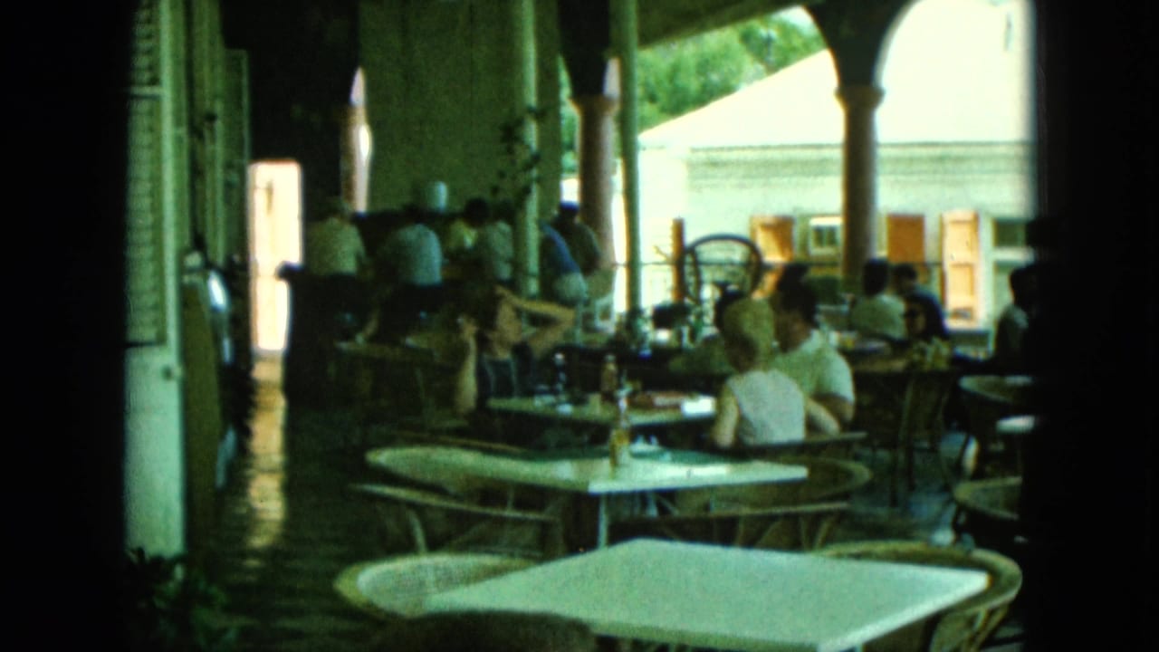Patrons seated at white patio tables under arched columns on a shaded terrace.
