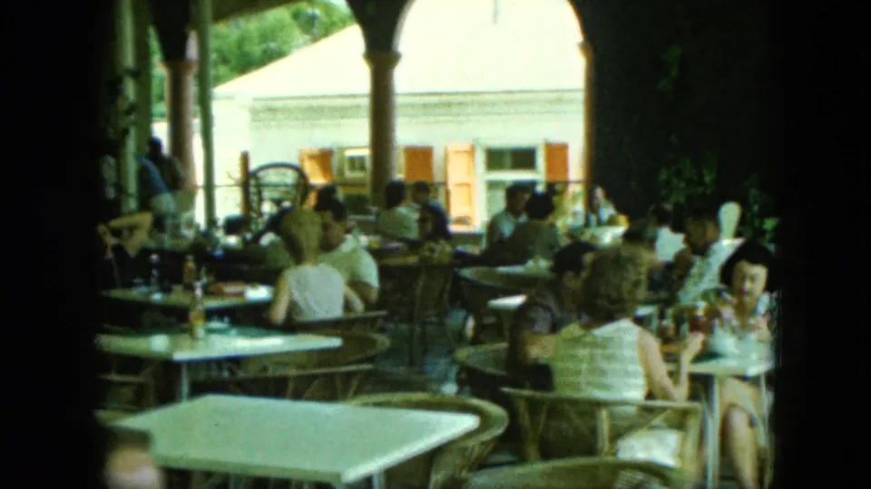 A closer home-movie view shows adults in summer clothing seated around tables on a covered patio.