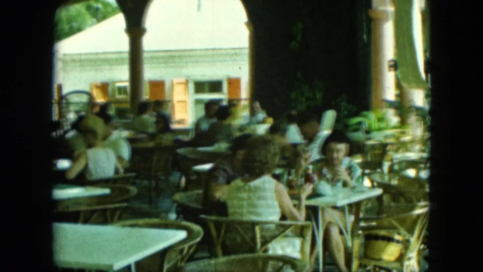 The final frame holds on the open-air dining terrace as patrons sit near columns and a sunlit exterior building.