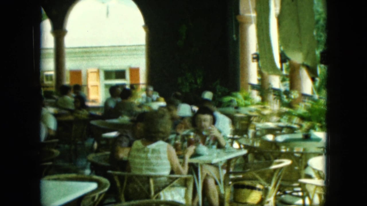 Two women sit at a café table while other diners fill the shaded arcade.